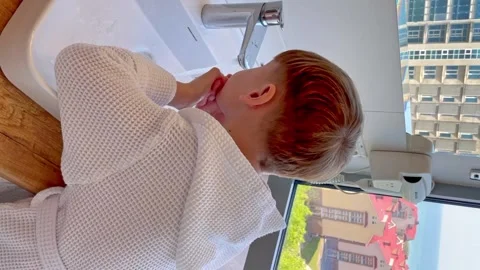 A child is brushing his teeth in the bathroom. A child in white hotel coat  Stock Footage 266169719