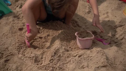 A child builds castles in a sandbox using a bucket and a shovel. Video stock 312048958