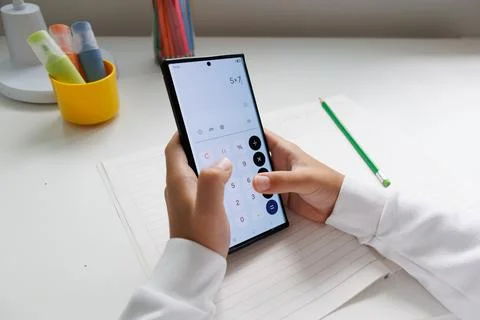 Child calculating a math problem with a smartphone calculator during homework Stock Photos