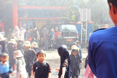 Child with calm expression while being sprayed with water by firefighters Stock Photos