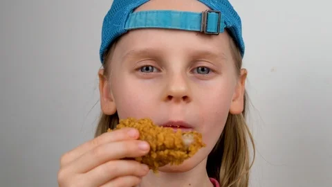 A Child in a Cap Eats a Chicken Leg has Fun and Laughs Looking at the Camera. Fa Stock Footage 126766370