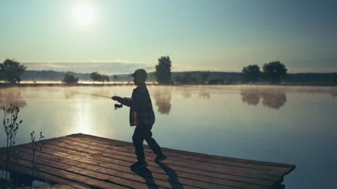 Child casting a spinning rod while fishing from a lakeside pier at sunrise 库存影片 340948466
