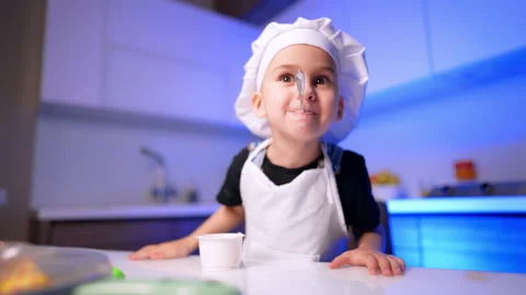 Child chef balancing spoon on face. A white cup sits on the glossy table as blue Stock Footage 343383740