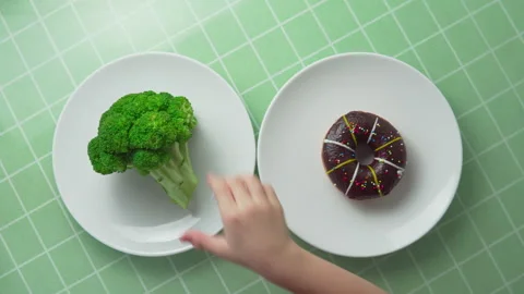 Child is choosing between broccoli and chocolate doughnut Stock Footage 263005271