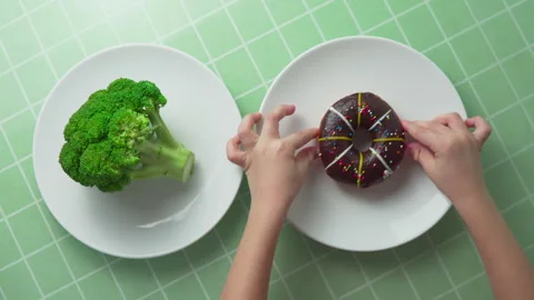 Child is choosing between broccoli and chocolate doughnut Stock Footage 264805886