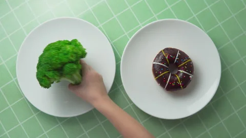 Child is choosing between broccoli and chocolate doughnut Stock Footage 274633522