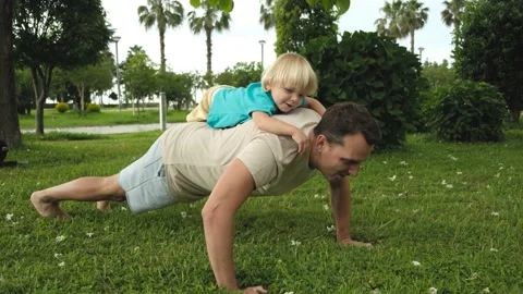 Child climbs on the father's back while father does push-ups from the floor in Stock Footage 200807019