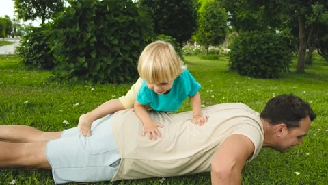 Child climbs on the father's back while father does push-ups from the floor in Stock Footage 200807415