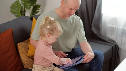A child with cochlear implants plays with a tablet computer with his father Stock Footage 181527964