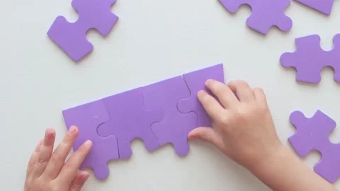 The child collects puzzle pieces while sitting at a white wooden table. Stock Footage 156869484