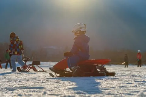 Child comes down from the mountain riding a red sled Stock Photos