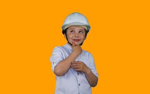 A child in a construction helmet with a pensive expression on an orange Stock Photos