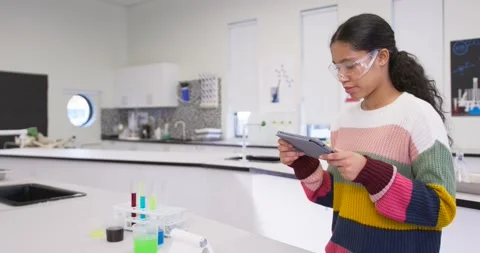 Child consulting tablet, following instructions and inspecting green tube on lab Stock Footage 340751768