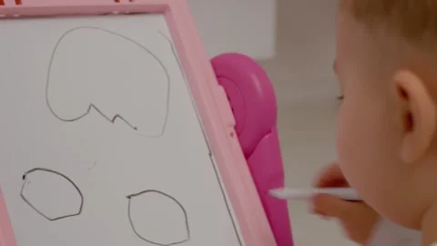 Child creates simple drawing on a pink board during playtime at home Stock Footage 329227281