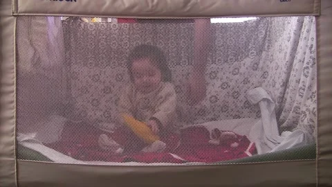 Child in crib seen through protective cloth, playing while father gives him Stock Footage 146520179