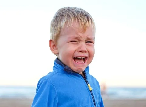 Child crying on the beach during a sunny day, expressing strong emotions wh.. Stock Photos
