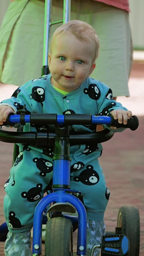 A child in a cute bear-patterned outfit rides a blue tricycle on a textured path Stock Footage 305896800