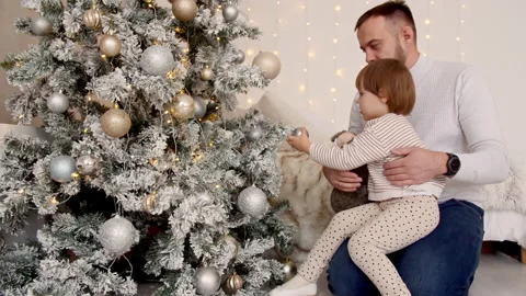 Child with dad decorates Christmas tree with balls on the background of bright Video stock 167432161