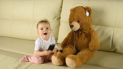 A child dances and laughs next to a toy bear in white headphones Stockbeeldmateriaal 147445283