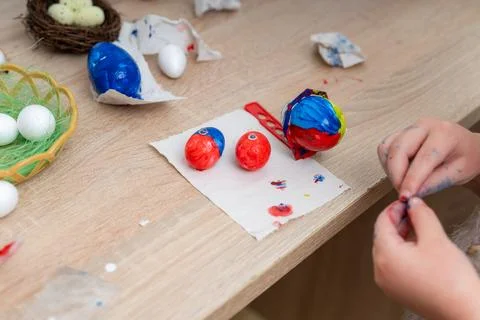 Child decorates easter eggs with colorful paints on a table at home 库存照片