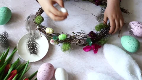 Child decorates an Easter wreath with decorative eggs, wooden table with tulips Stock Footage 265422621