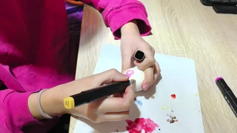 Child decorates egg with pink marker and colorful paints on wooden table during Stock Footage 328438700