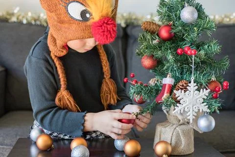 Child decorating Christmas tree with balls and snowflakes wearing dress and s Stock Photos