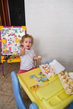 Child decorating egg for Easter holiday. Toddler sitting at table with art Stock Photos