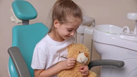 Child dentist examining the teeth of a teddy bear with a mirror Stock Footage 307460146