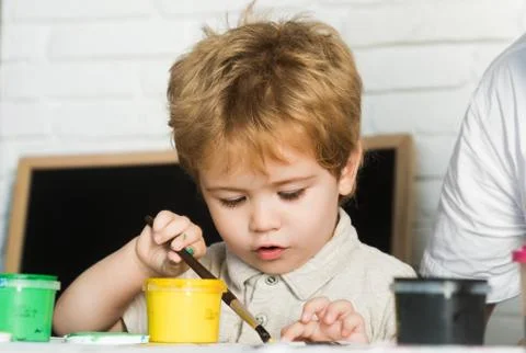 Child development, boy draws paint yellow with brush, interest in art Stock Photos
