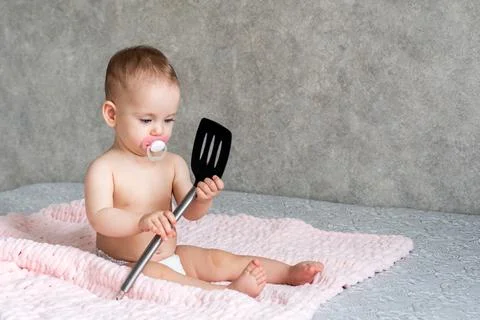 The child develops with interest while playing with a kitchen spatula Stock Photos