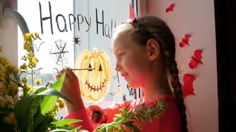 Child in devil horns painting pumpkin on window preparing celebrate Halloween Stock Footage 160955909