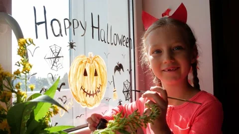 Child in devil horns painting pumpkin on window preparing celebrate Halloween Stock Footage 160959692
