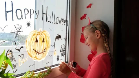 Child in devil horns painting pumpkin on window preparing celebrate Halloween Stock Footage 160963879