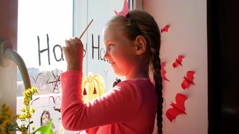 Child in devil horns painting pumpkin on window preparing celebrate Halloween Stock Footage 161012175