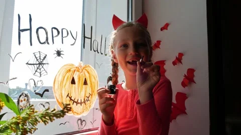 Child in devil horns painting pumpkin on window preparing celebrate Halloween Stock Footage 161012809