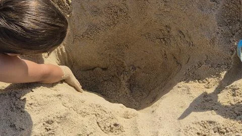 A child digging a deep hole in the sand at the beach Stock Photos