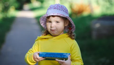 A child is on a dirt path surrounded by greenery. She holds a blue container  Foto stock