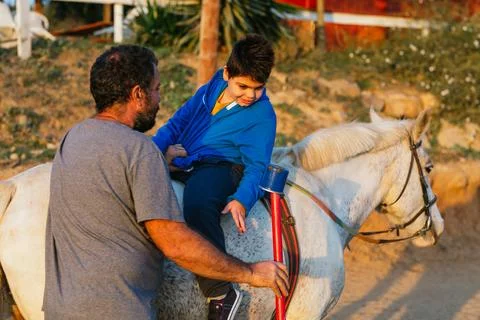Child with disabilities doing an exercise during an equine therapy session with Stock Photos