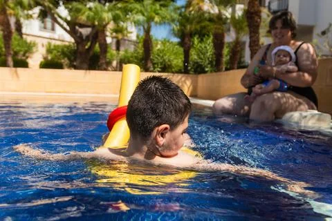 Child with disability swimming in pool with floatation device, mother and baby Stock Photos