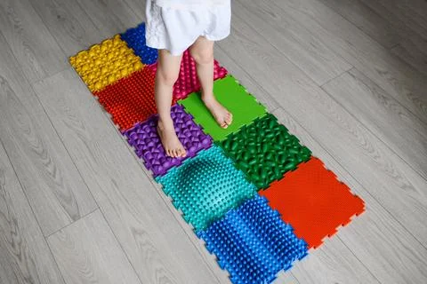 The child does exercises on an orthopedic multi-colored foot massage mat Stock Photos