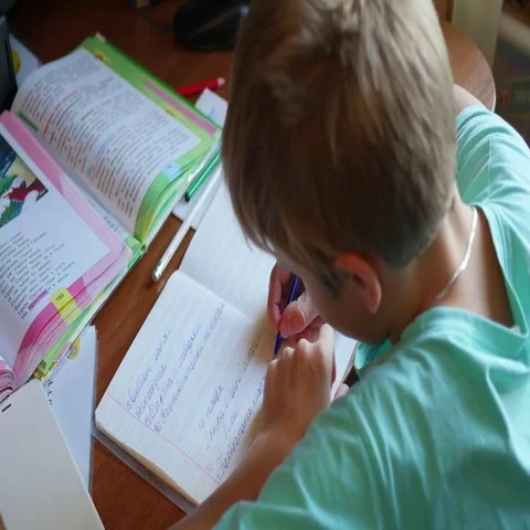 The child does his homework, writes in a copybook at table Vidéo 69435332