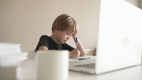 A child does homework using a laptop while sitting at home in the kitchen at the Stockbeeldmateriaal 142031876