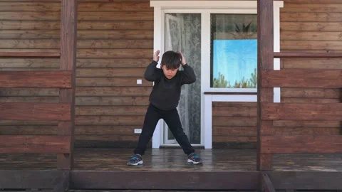 A child does morning exercises standing on the veranda A small boy does sports Stock Footage 153928769