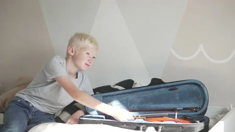 The child does not want to do violin at home, the boy sits on the bed by the Stock Footage 162256496