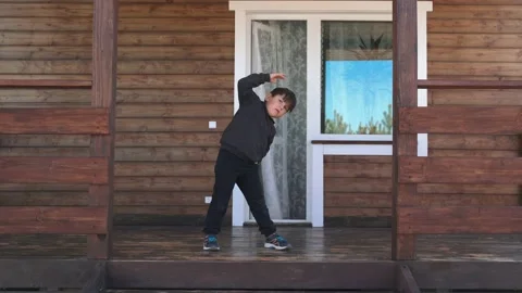 As a child doing exercises performing bends to the sides standing on the veranda Stock Footage 153852218