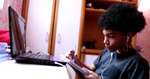 Child doing homework at home in front of laptop. Black ethnicity kid writing  Stock Footage 144342390
