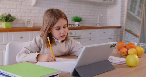 Child doing homework at kitchen table, watching lesson on tablet, using Stock Footage 314967121