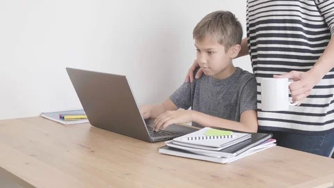 Child doing homework with laptop computer. Mother come to support him Stock Footage 127880497