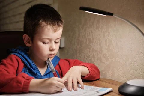 Child Is Doing Homework In The Light Of The Lamp In The Evening. A Boy Sits a Stock Photos